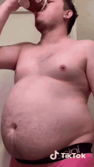 a shirtless man with a very large belly is drinking from a glass .