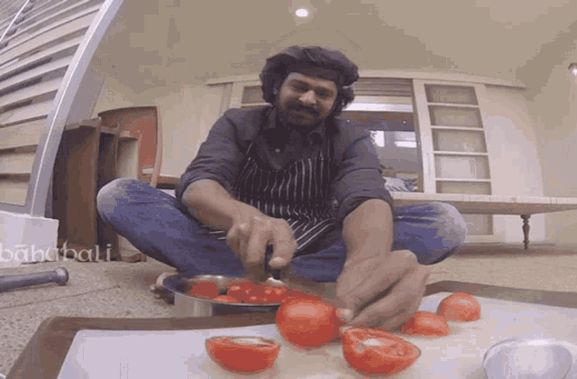a man is sitting on the floor cutting tomatoes with the word bahabali visible in the background