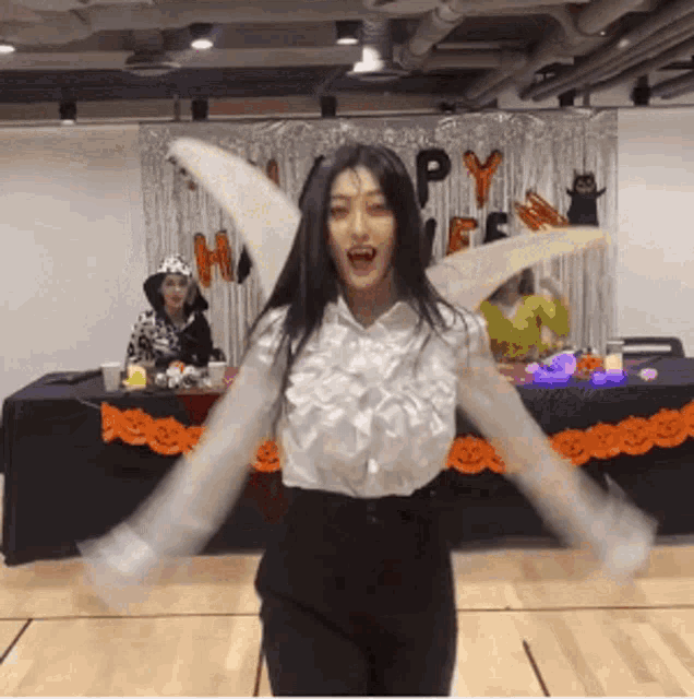 a woman in a white shirt and black pants is standing in front of a table with a happy halloween sign