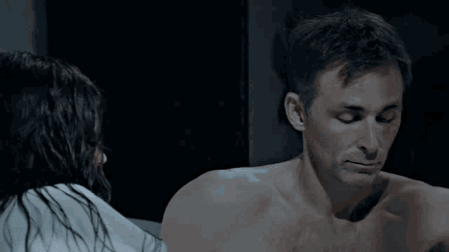 a man without a shirt is looking at a woman in a dark room