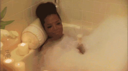 a woman is taking a bath in a bathtub with candles on the side