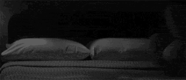 a black and white photo of a bed with pillows and a blanket .