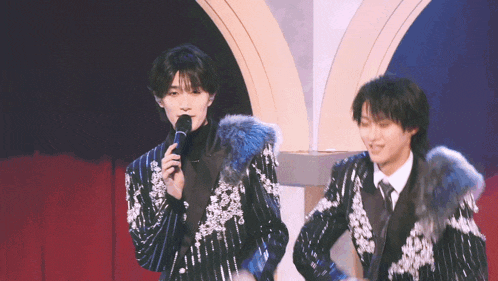 a man holding a microphone stands next to another man in a suit