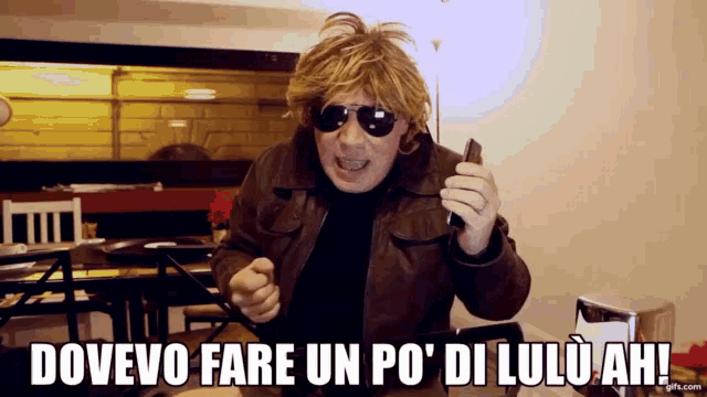a man wearing sunglasses holds a cell phone and says dovevo fare un po di lulu ah