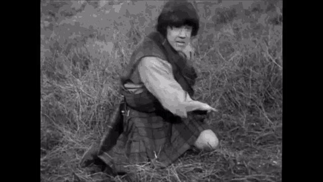 a man in a kilt is kneeling in the grass .