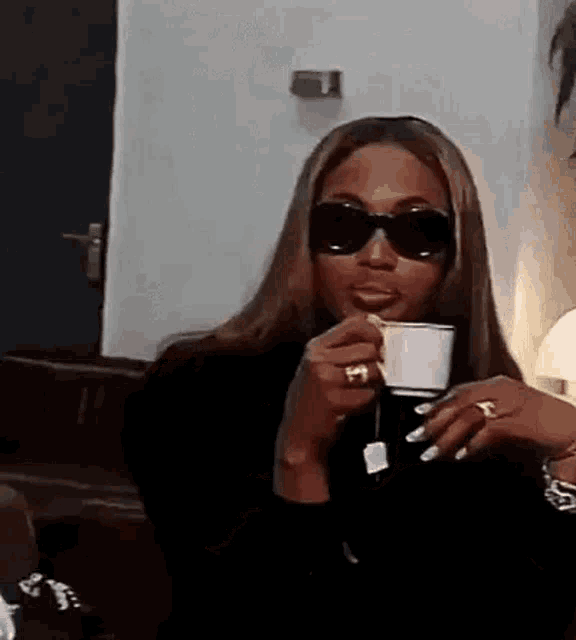 a woman wearing sunglasses is holding a cup of coffee in her hand .