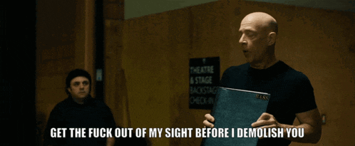 a bald man is pointing at a sign that says theatre stage backstage