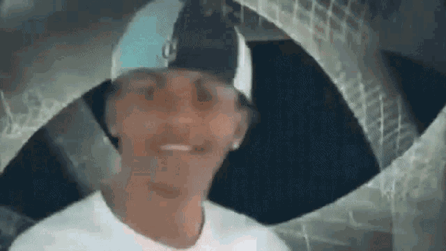 a man wearing a hat and sunglasses is smiling in front of a brick wall .