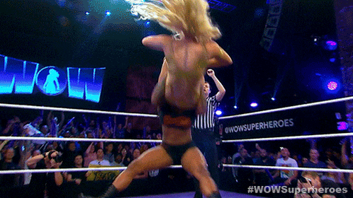 a woman in a wrestling ring with #wowsuperheroes written on the wall