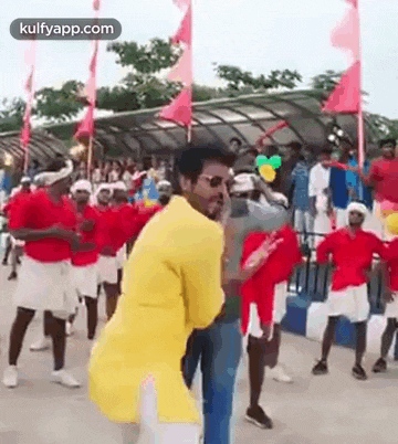 a man in a yellow shirt is dancing with a group of people in red shirts .