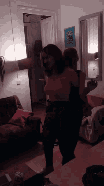 two women are dancing in a living room with a picture on the wall