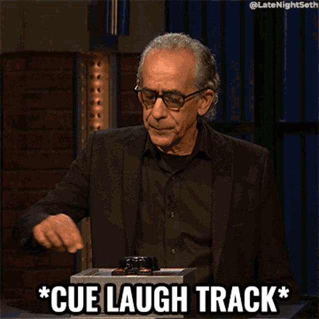 a man in a suit is pressing a button and says cue laugh track
