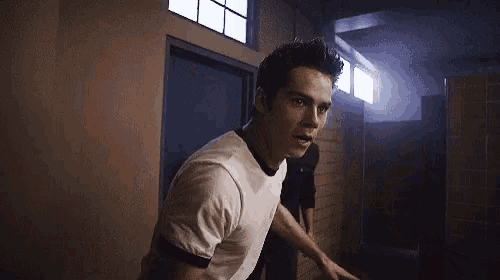 a man in a white t-shirt is walking down a hallway next to another man .