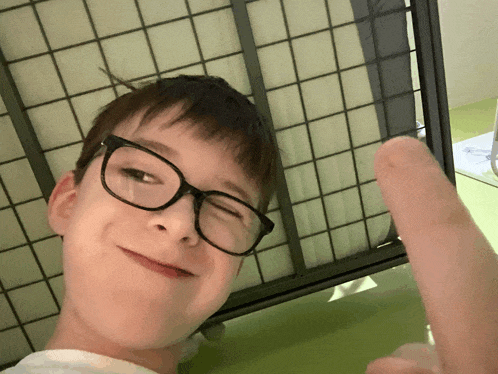 a young boy wearing glasses is giving a thumbs up sign