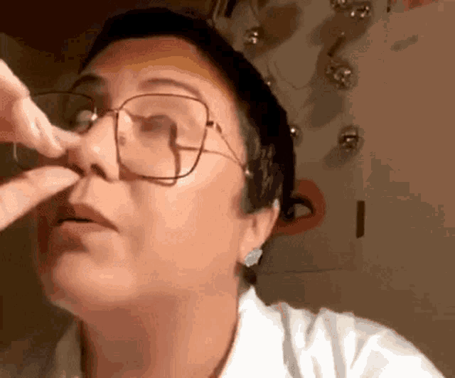 a woman wearing glasses is cleaning her nose with her finger .