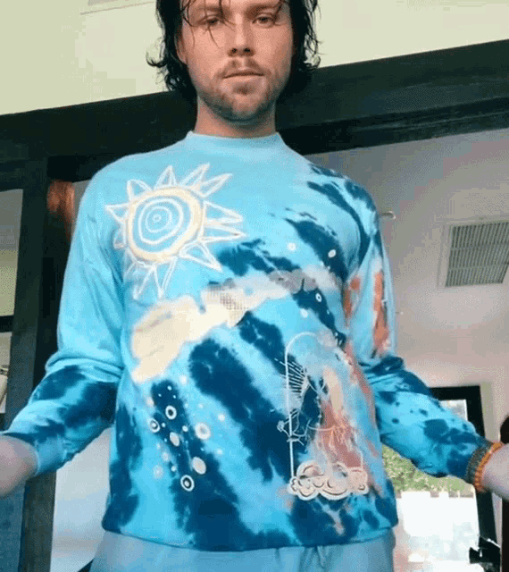 a man is wearing a blue tie dye shirt with a sun and clouds on it