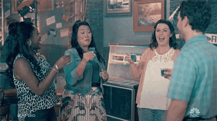 a group of people are standing in a room talking to each other while holding drinks .