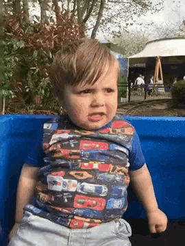 a little boy wearing a shirt with cars on it is sitting in a blue wagon .