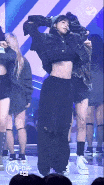 a woman is dancing on a stage in front of a crowd while wearing a crop top and a hat .