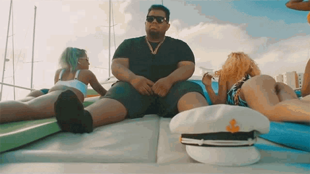 a man sits on a boat with two women laying on the back