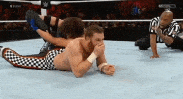 a wrestler is laying on the ground in a wrestling ring while another wrestler is laying on the ground .