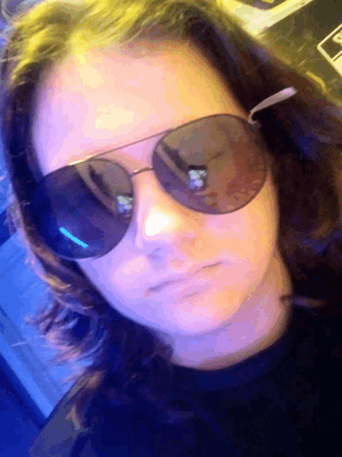 a woman wearing sunglasses looks at the camera with a serious expression