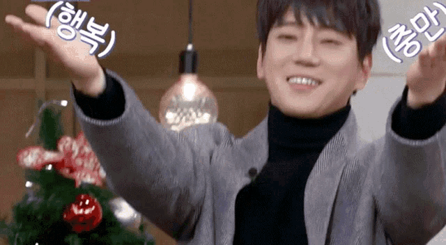 a man with his arms outstretched in front of a christmas tree with asian writing on it