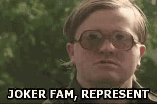 a man wearing glasses is saying `` joker fam , represent '' while standing in front of a tree .