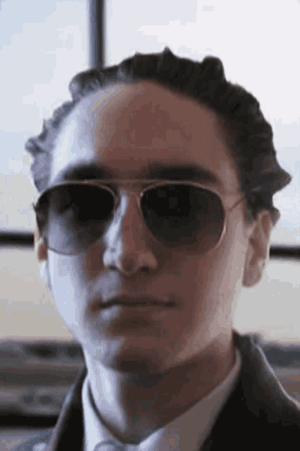 a young man wearing sunglasses and a suit looks at the camera