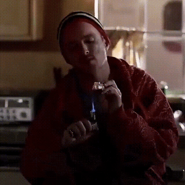 a man in a red jacket is lighting a cigarette with a lighter in a kitchen .