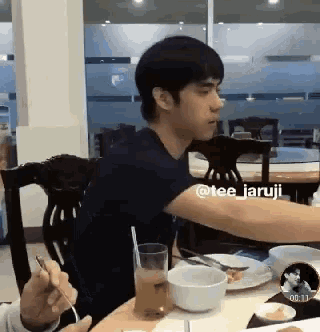 a man in a black shirt is sitting at a table with a glass of orange juice and a bowl of food ..