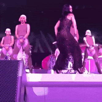 a woman in a black dress is dancing on a stage with a group of dancers behind her .