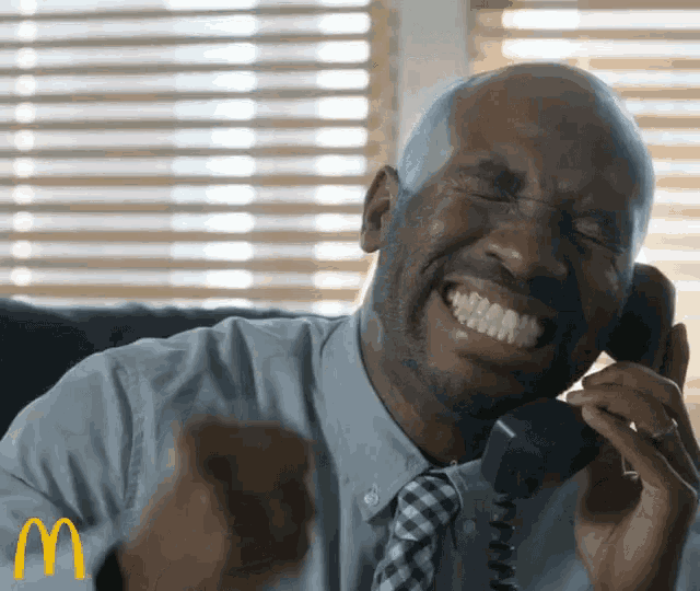 a man is laughing while talking on a telephone with a mcdonald 's logo in the corner