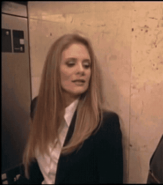 a woman in a suit and white shirt is standing in front of a wall with a sign on it that says ' a '