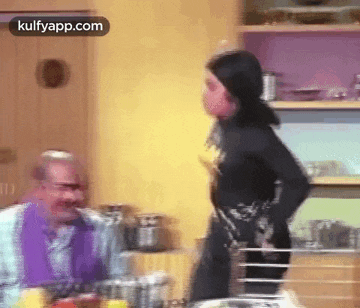 a woman is standing in front of a man in a kitchen .