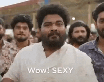 a man with a beard is standing in front of a crowd of people and says wow ! sexy .