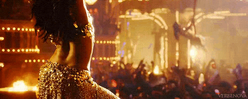 a woman in a gold dress is dancing in front of a crowd in a dark room .