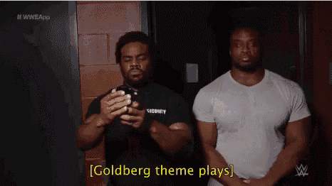 two men are standing next to each other and one is holding a cell phone and the other is saying goldberg theme plays