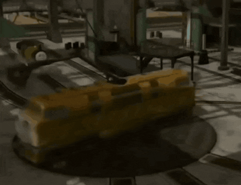 a yellow toy train is on a turntable in a factory