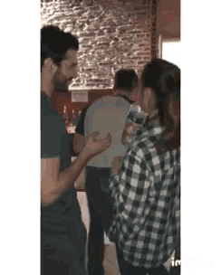 a woman in a plaid shirt is holding a bottle of water while standing next to a man in a black shirt .