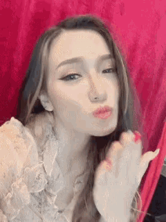 a woman is blowing a kiss at the camera while wearing a white top .