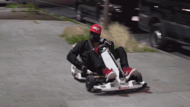 a man in a red hat is riding a go kart on a road