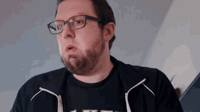 a man with glasses and a beard is wearing a black shirt that says ' x '