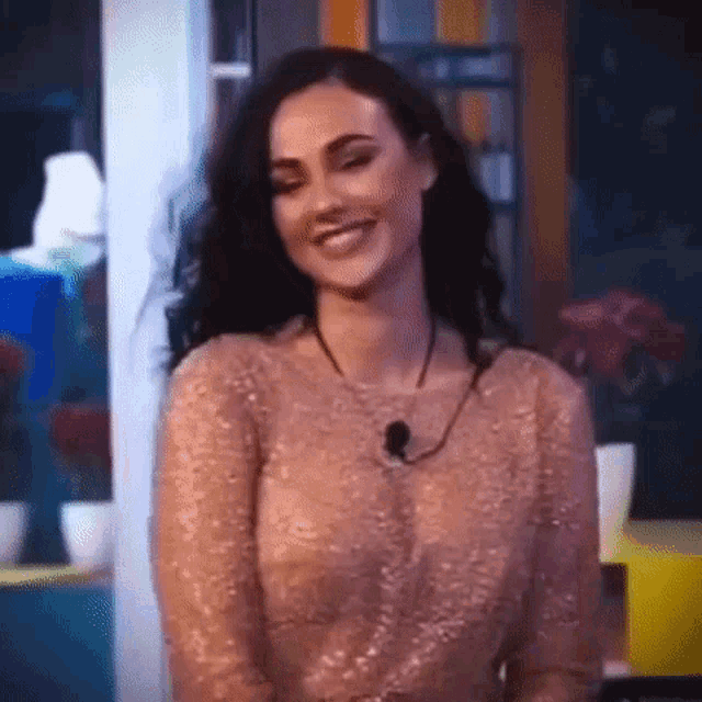 a woman in a sequined dress is smiling and looking at the camera while wearing a necklace .