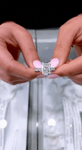 a woman with pink nails is holding a diamond ring in her hands