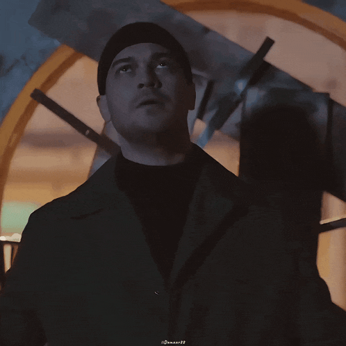 a man wearing a black beanie and a black coat looks up at something