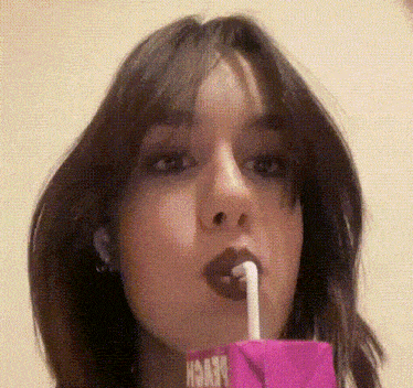 a woman drinking from a pink box with the word peach on it
