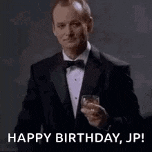 a man in a tuxedo is holding a glass of whiskey and saying happy birthday , jp .