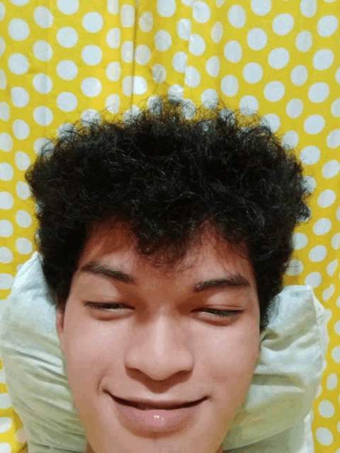 a young man with curly hair is laying on a bed with his eyes closed
