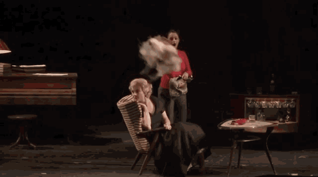 a woman in a red sweater throws a piece of cloth over another woman in a chair